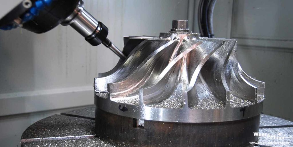 CNC machine milling a metal turbine component with metal shavings visible.
